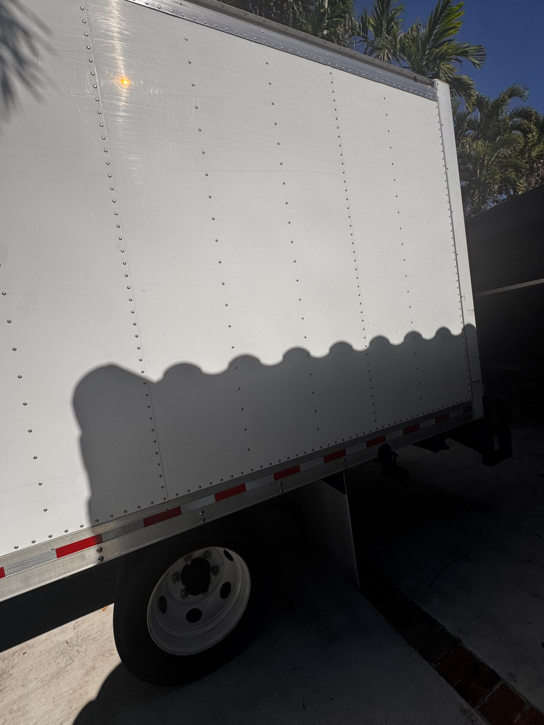 Box truck trailer side panel with riveted aluminum siding and wheel visible at bottom; no identifying text visible.