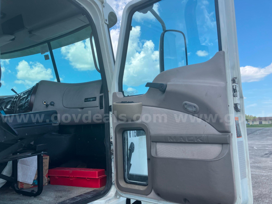 Cab and chassis truck interior showing open door with MAEKI panel, dash area, and steering wheel. Passenger door window visible, light gray interior with beige panels.