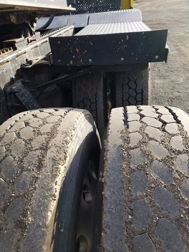 Peterbilt truck dual rear wheels with cracked tread and surrounding mud, rear axle area and step/frame visible.
