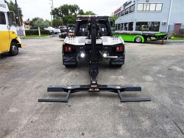 Ram 4500 SLT tow truck rear view with hydraulic hitch and front mount, black frame, metal platform, dealership lot in background.