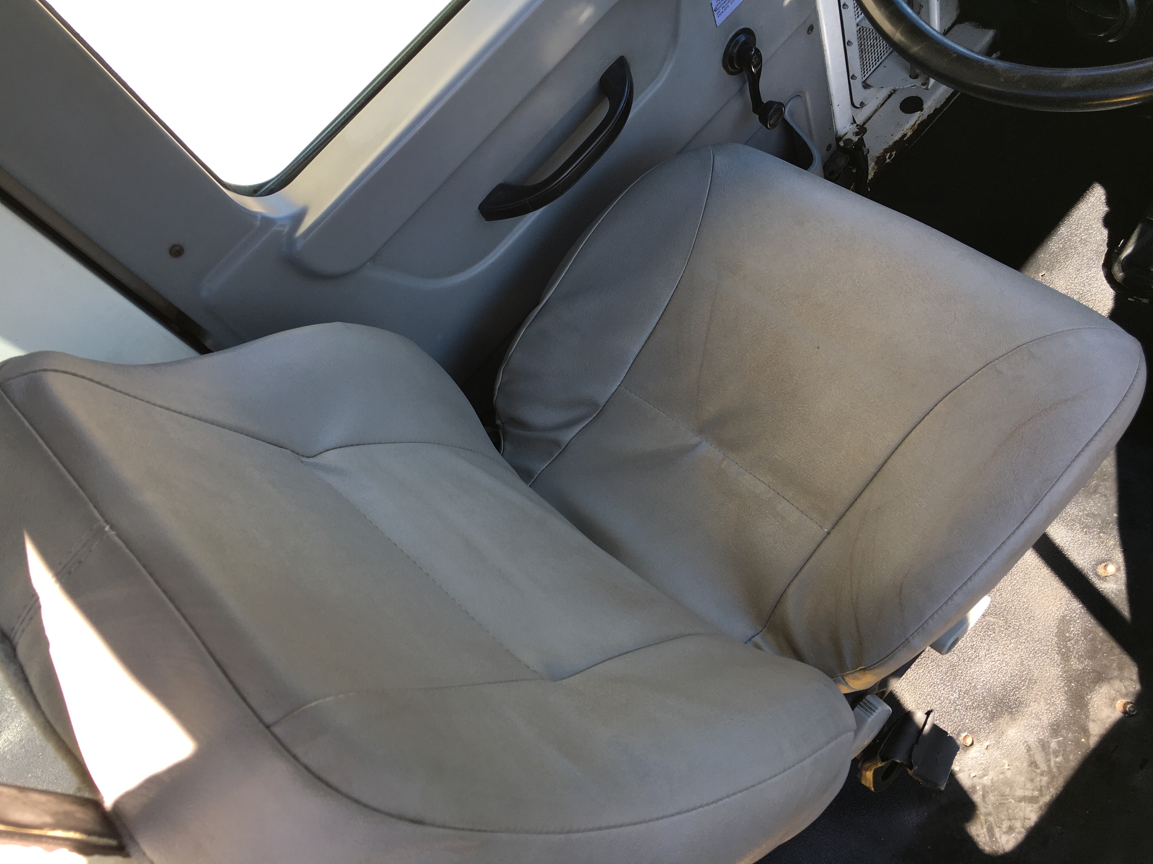 Cab interior showing two light gray seats in a Kalmar Ottawa YT30 yard truck with a black steering wheel and door handle visible.