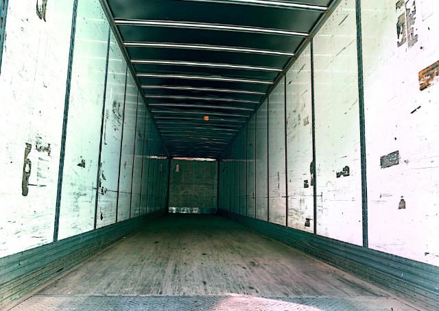 Interior of an empty cargo trailer with white sidewalls and a wooden floor, viewed from the back.