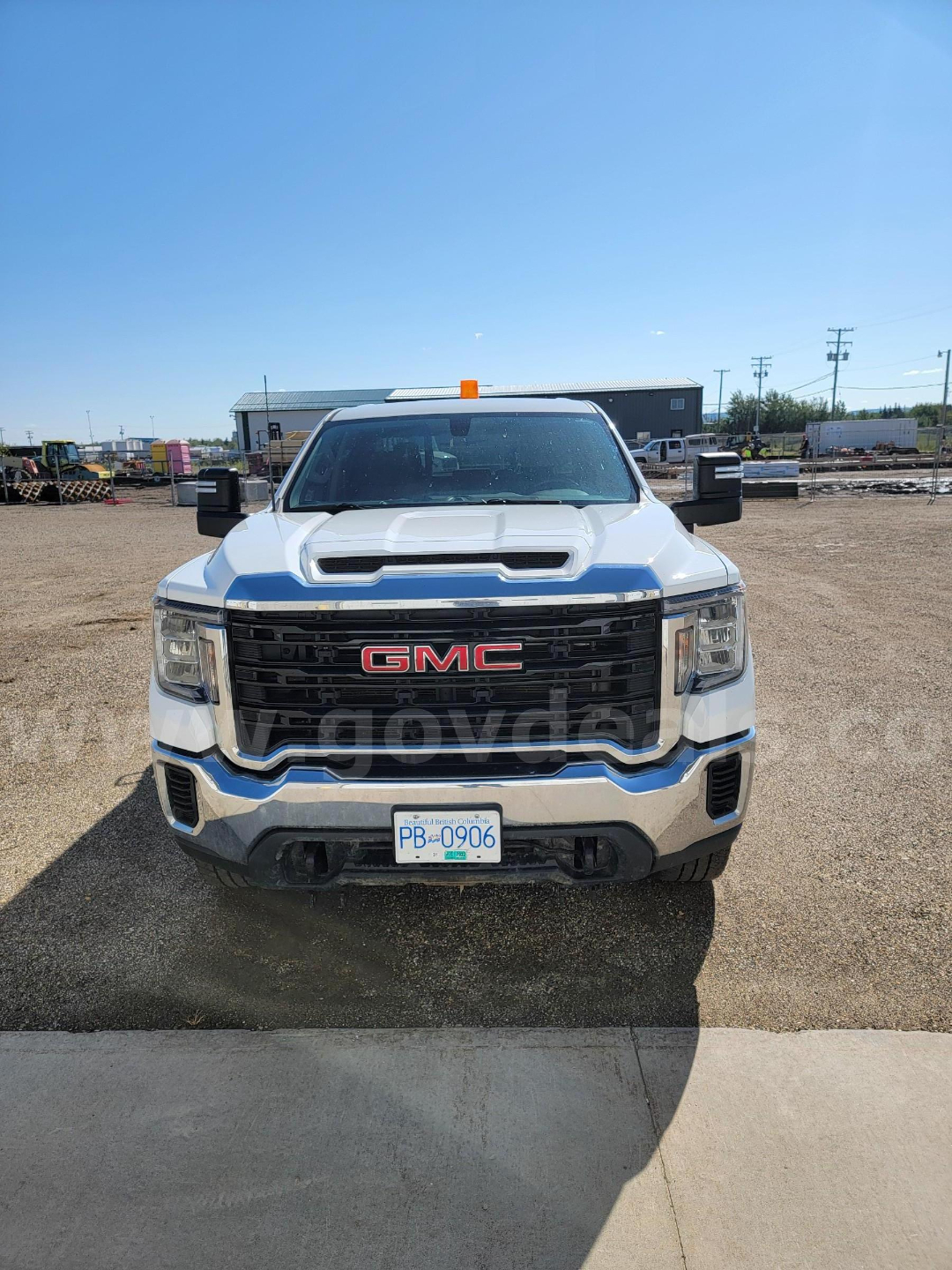 GMC Sierra 3500HD front view showing bold black grille with red GMC emblem and chrome bumper. White crew cab with orange beacon on roof, Alberta license plate visible.