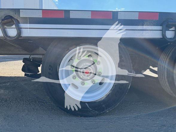 Trailer wheel and frame with decorative watermark of two hands and a bird overlay; no legible labels or fluid markings visible on the trailer.