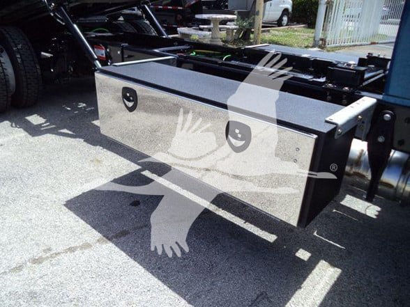 Truck chassis with a large rectangular storage box mounted under the cab, side view showing lid and mounting brackets.