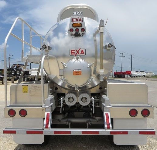 EXA vacuum tank trailer rear view with circular stainless tank, EXA logos, ladder, dual rear hoses, and taillights.
