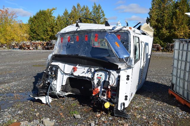 Damaged cab of a white 2017 Western Star 5700 XE truck with missing front end and exposed engine bay, windshield shattered, and debris around.