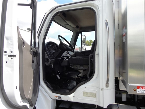 Truck cab interior of a Freightliner BUSINESS CLASS M2 106 with open door, showing steering wheel, dashboard, and driver's seat.