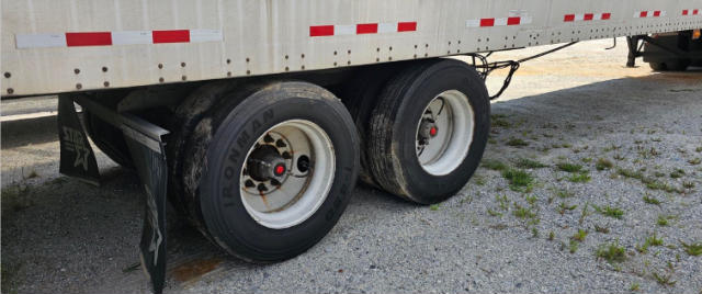 Dual rear trailer wheels with Ironman tires and white rims under a Vanguard VXP trailer; visible is a portion of the side with red and white reflective tape.