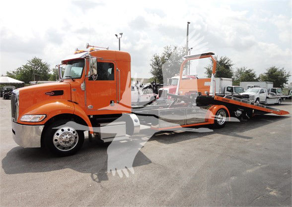 Orange 2022 Peterbilt 337 tow truck with flatbed trailer in a dealership lot.