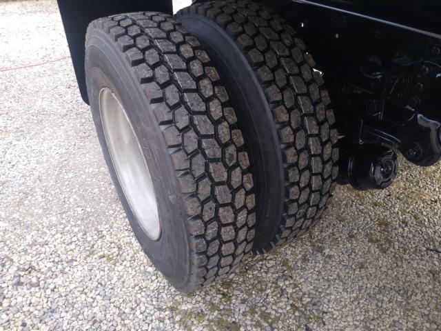Truck dual rear wheels with large off-road style tread on gravel surface; visible parts include wheel rims and suspension components.
