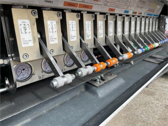 Close-up of a trailer control panel with multiple gauges and valves, labels, and colored handles in a row.