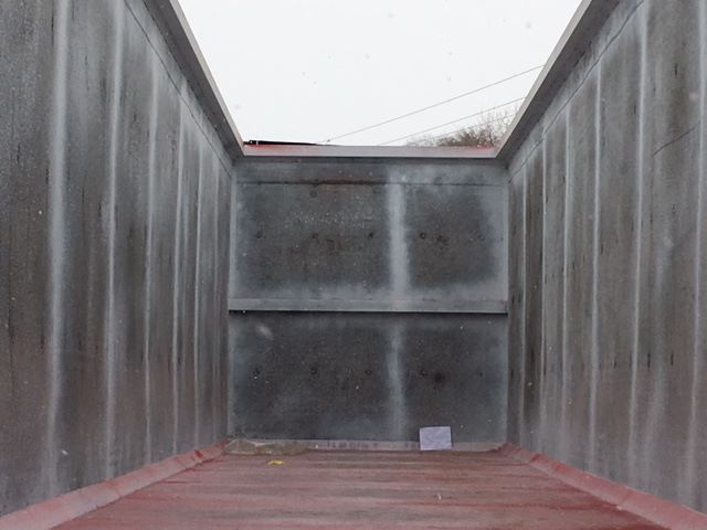 Interior of a scrap gondola trailer with metal walls and a red floor, view from the back end looking toward the open top.
