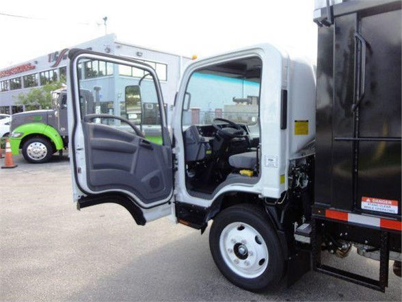 Isuzu NPR HD cab open showing driver door and interior, white truck with black dump body attached.