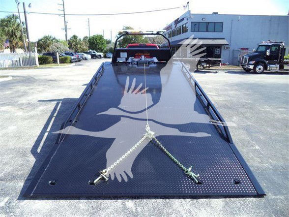 Ram 5500 tow truck flatbed loading ramp area with chains securing a vehicle, seen from front of bed, dealership lot in background.