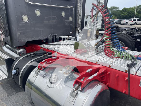 Peterbilt 389 truck chassis showing cylindrical fuel/tank and red frame with coiled air hoses and metal diamond plate steps.