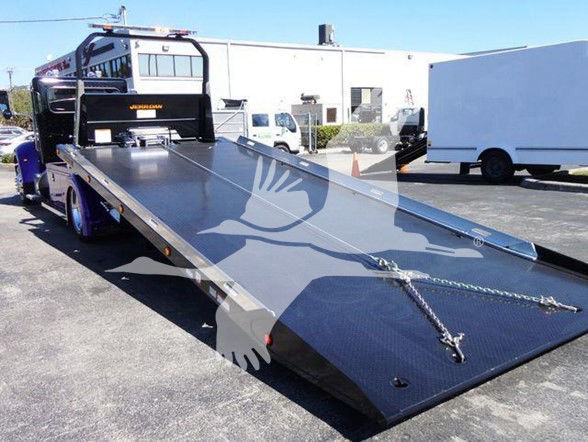 Peterbilt 337 flatbed tow truck with ramp extended, black cab, and chain strap on the ramp.