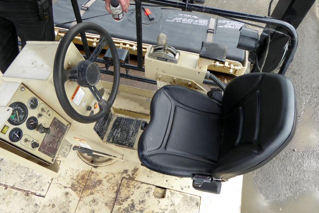 Ingersoll-Rand DD110 truck interior showing steering wheel, gauges, and a black seat. Instrument cluster and control panel visible; beige metal floor with wear.