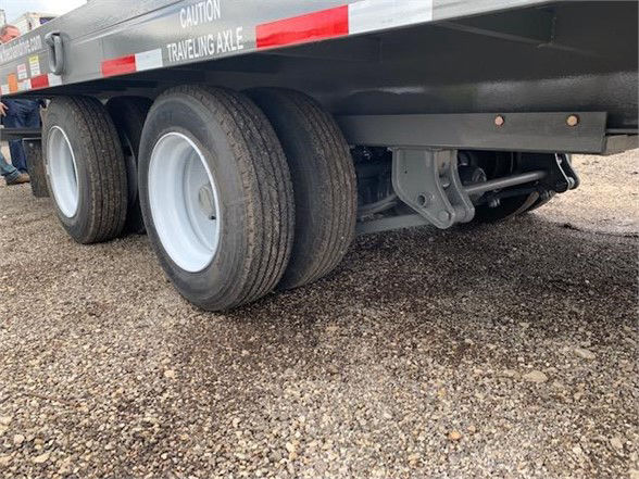 Trailer undercarriage showing tandem axle wheels on a tan container delivery trailer with CAUTION traveling axle markings and suspension components.