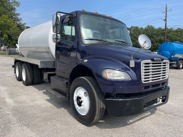 Freightliner M2 vacuum/sewer truck with dark blue cab and silver cylindrical tank, side view showing front grille and side mirror.