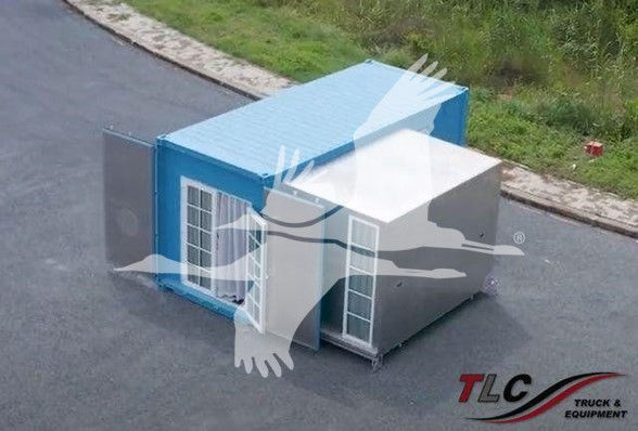 Trailer unit with blue and gray modular structure showing doors and windows, on paved surface.