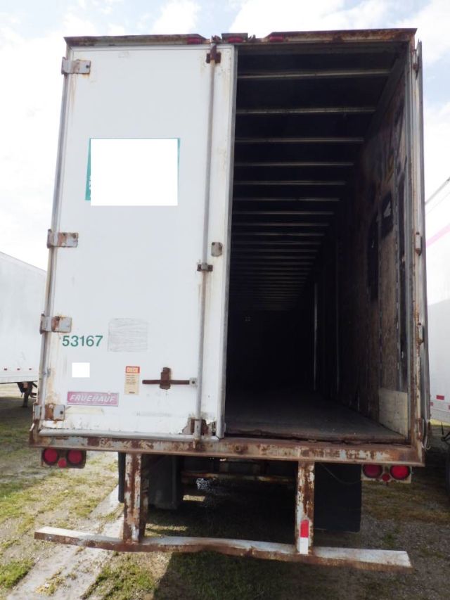 Open back of a white Fruehauf storage trailer with interior visible, rust on lower frame, rear lights, and license stickers.