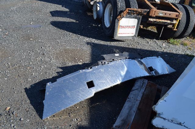 Side-view of a damaged metal truck bumper panel on gravel with a Western Star truck trailer chassis in background.
