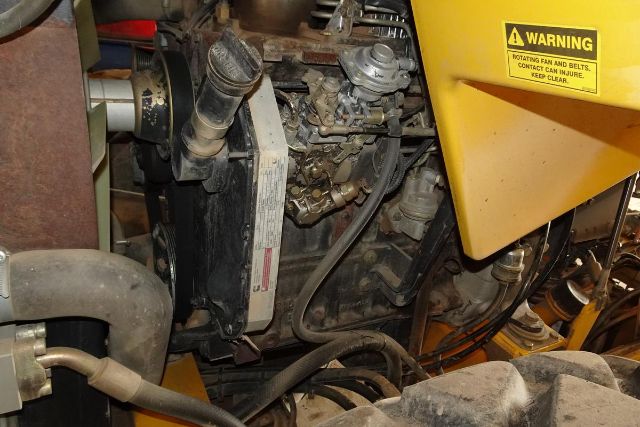 Vibromax VM106D engine bay showing radiator, hoses, hydraulic components, and warning label on yellow panel.