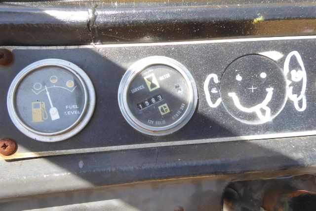 Caterpillar V225 dashboard gauges showing fuel level, service/idle indicator, hour meter, and smiling face doodle on metal panel.