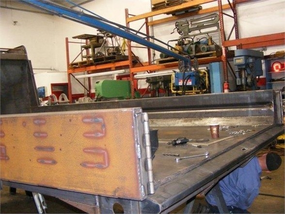 Welding shop with a flatbed dump body in progress. Visible text includes stock number 14 YARDBIRD and category truck parts.