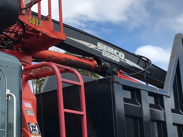 Peterbilt 388 grapple truck with Serco 3500 crane arm and hydraulic hoses. Visible text on equipment includes 'SERCO 3500' on the crane arm and a red ladder in foreground.