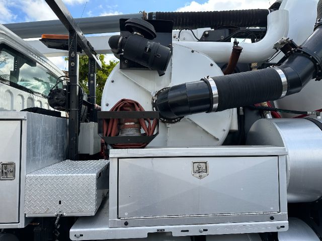 Freightliner M2 vacuum truck side view showing large exhaust/air intake hose, metal storage boxes, and tool compartments.