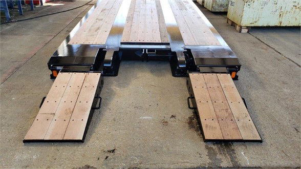 Lowboy trailer deck with wooden ramps extended, showing the loading platform and support rails.