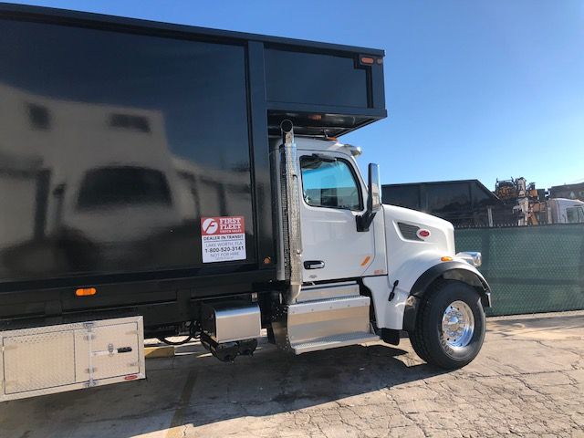 2018 Peterbilt 567 grapple truck side view showing cab, chrome steps, and black dump body. Visible sticker on black body near cab with text.