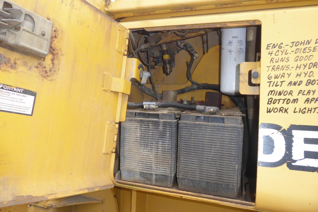 Dozer/crawler tractor engine bay showing two large battery boxes and hydraulic lines inside yellow housing.