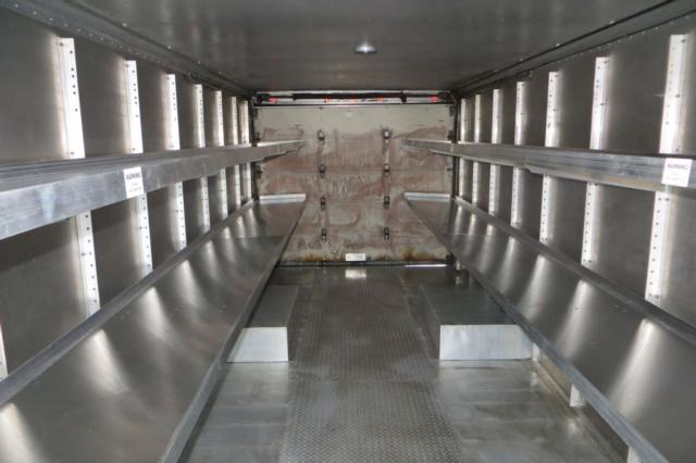 Interior of a Freightliner MT45 cargo area with metal shelves along both sides and a rear double-door opening.