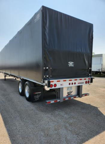 Trailer rear view of a 2020 Manac COMBO flatbed trailer with a black tarp, dual rear wheels, and stock number 2023717 visible.