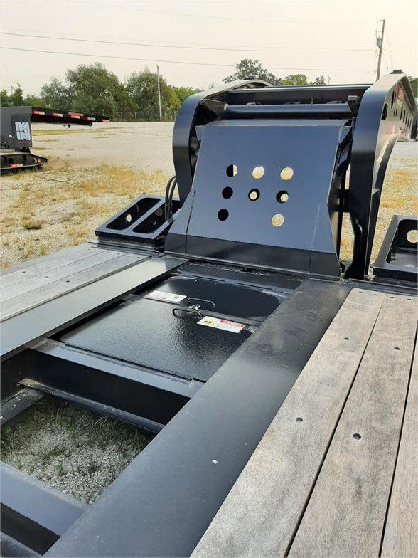Flatbed lowboy trailer deck with hydraulic gooseneck and circular cutouts on rear riser. Steel frame, wooden deck sections, attachments, and storage pockets.