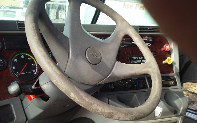 Truck interior showing steering wheel and dashboard with gauges, labels, and controls. Visible text includes 'TRUCK MUST BE IN NEUTRAL BEFORE' and various dashboard stickers.