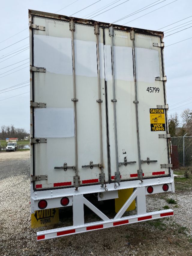 Rear view of a 2002 Wabash Duraplate trailer with double doors, metal latches, and warning decals; yellow 'Caution: Wide Turns' sign and rear underrun protection.