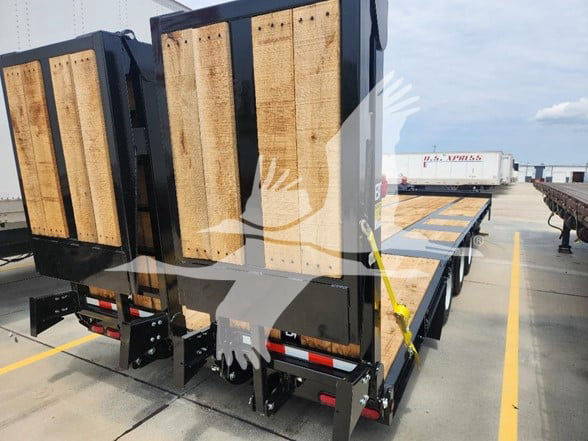 Trailer flatbed with wooden side rails and loading ramps, on a multi-axle trailer at a loading area.