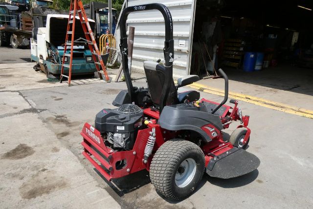 Ferris IS 700Z stand-on mower in red with black seat and roll bar, gas engine, large front caster wheels, and slick rear tires parked outside a garage.