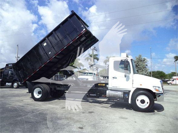 [Truck] white 2016 Hino 268A dump truck with bed raised in a dealer lot. Visible text includes VIN 5PVNJ8JT6G4S57015 and stock number T57015.