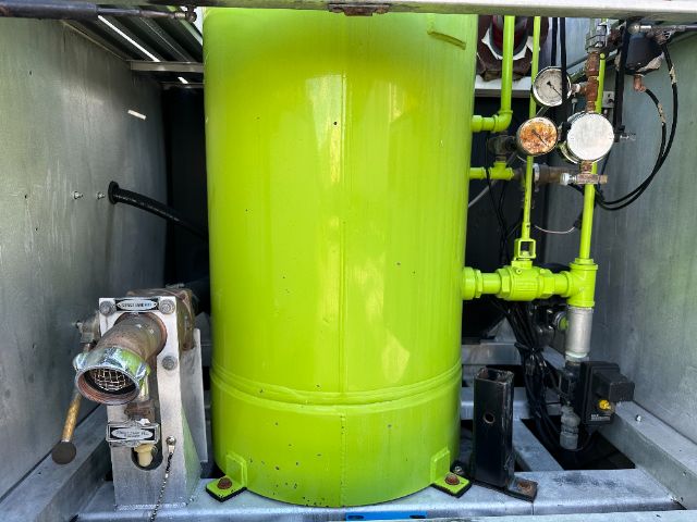 Green cylindrical fire pump system with gauges and piping mounted inside a metal compartment. Large lime-green tank center, with valve gauges and connectors on right, and a metallic actuator on left.