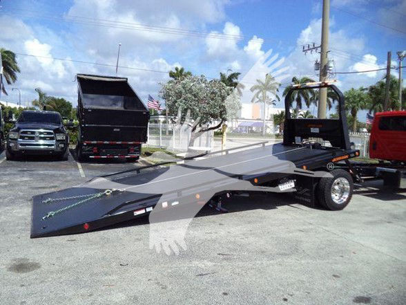 Tow truck flatbed with a low-profile car hauler and a wheel lift at the rear, black frame, and a matte gray bed in a dealership lot.