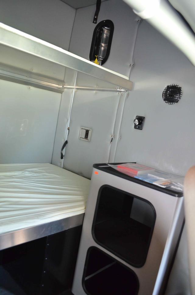 cab interior of a 2014 Kenworth T370 with a small bed, shelf, and storage cabinet in a box truck.