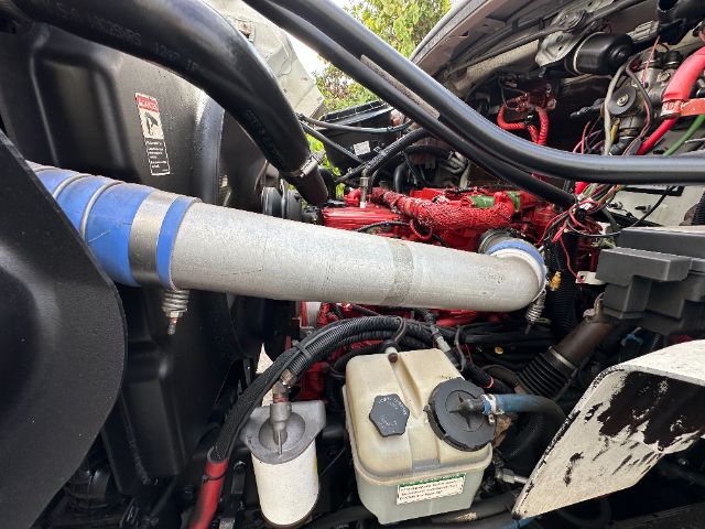 [Component] [Front engine bay] showing air intake tube, coolant reservoir, power steering fluid reservoir, and various hoses in a Freightliner M2 engine compartment.