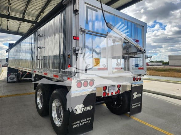 Dump trailer showing metal sided dump with dual rear wheels and Travis branding on mud flaps.