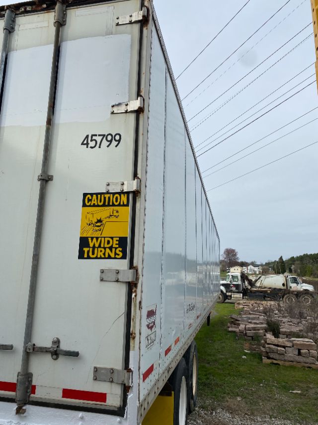 Trailer side door showing '45799' number with CAUTION WIDE TURNS sticker on a white Wabash Duraplate trailer.