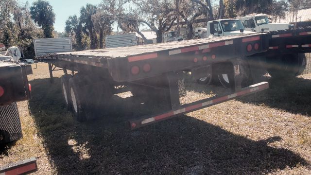 Flatbed trailer showing rear and side with dual axle configuration and taillights.
